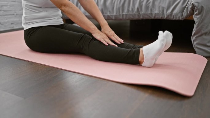 容光焕发的女人坐在卧室地板上，她的手伸展腿，同时冥想，作为早晨醒来的平衡和健康锻炼。