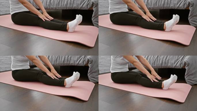容光焕发的女人坐在卧室地板上，她的手伸展腿，同时冥想，作为早晨醒来的平衡和健康锻炼。