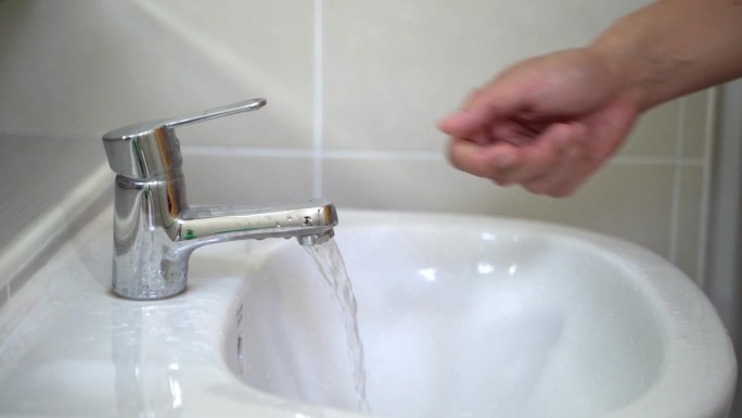 男子的手打开水龙头，在浴室洗脸盆洗手。清洁健康的理念。