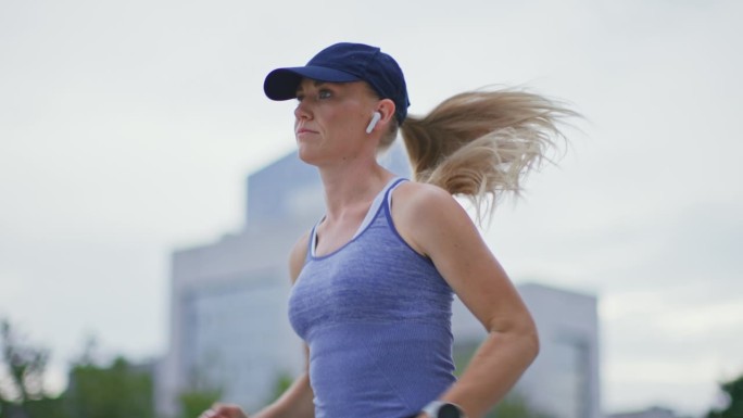 SLO MO TS Fit金发女子戴着棒球帽，在城市跑步