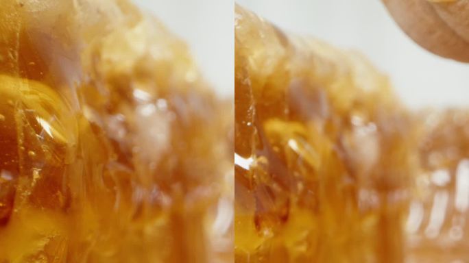 在一个充满蜂蜜的环境中，镜头在木勺下和蜂巢之间移动，从木勺上滴下蜂蜜。垂直视频。