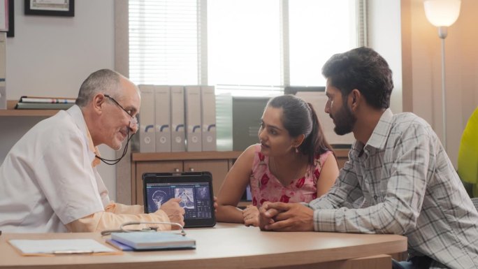 印度夫妇在私人诊所看医生:专业医生使用数字平板电脑向患者解释核磁共振成像结果，回答问题，建议最佳医疗