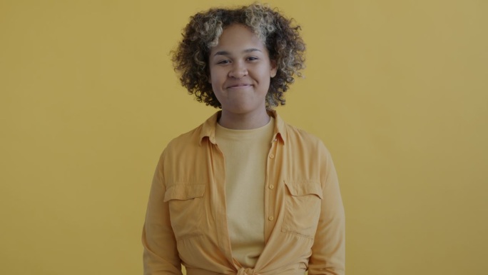 在黄色背景上，一个欢快的非裔美国女士点头表示同意，微笑着感到乐观的慢动作肖像