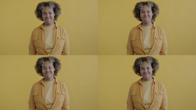 在黄色背景上，一个欢快的非裔美国女士点头表示同意，微笑着感到乐观的慢动作肖像