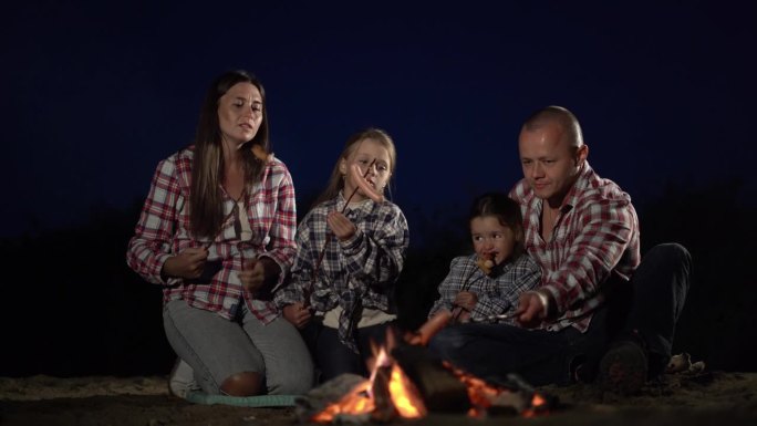 深夜，一家人在湖边露营，在篝火里煮香肠