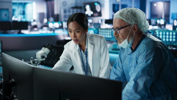 医院研究实验室会议:女性亚洲神经科学家与男性高加索神经外科医生讨论在台式电脑上进行CT脑部扫描。穿着