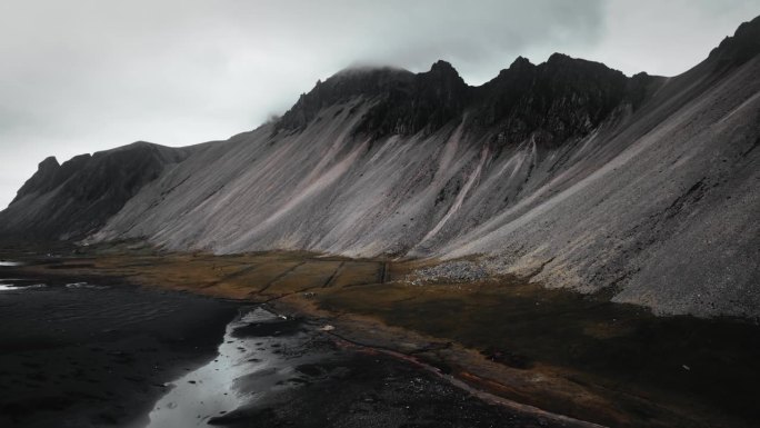 空中黑色的沙滩沙滩，黑色的火山山脉，绿色的橙草，黑暗忧郁多云的景色，冰岛