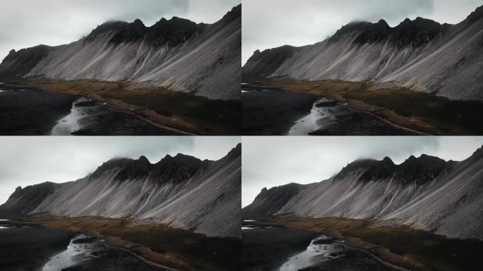 空中黑色的沙滩沙滩，黑色的火山山脉，绿色的橙草，黑暗忧郁多云的景色，冰岛