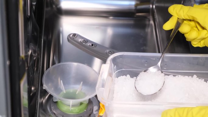 一个女人把盐倒进洗碗机里清洗。洗碗