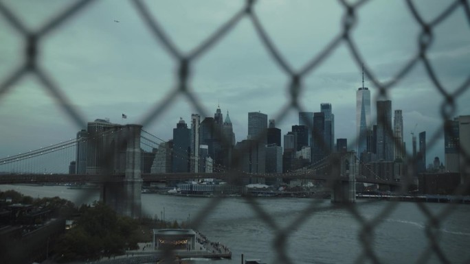 东河上标志性的纽约市景观，摩天大楼和布鲁克林大桥。电影傍晚城市天际线与日落和多云的天空。围栏后面的镜