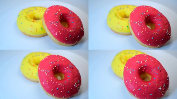 两个甜甜圈在白色的背景上旋转，上面有黄色和粉色的釉面，还有香蕉和草莓口味的彩色糖屑。