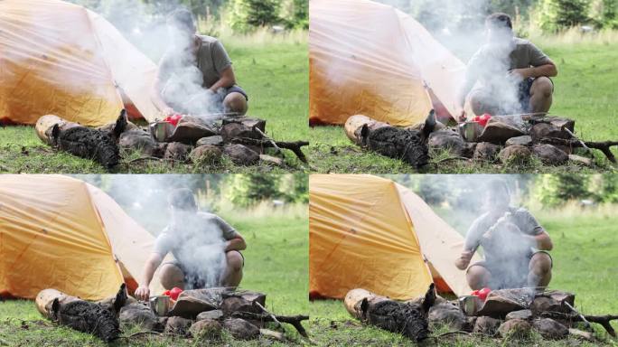 一个人在帐篷附近准备美味的烤肉串。用大量的烟烤串的过程。在大自然中烹饪。