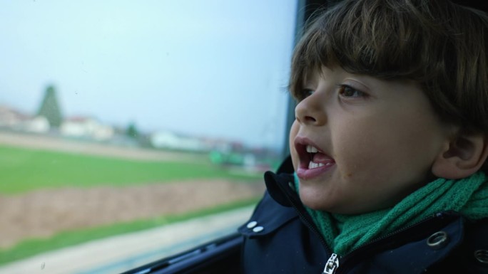 兴奋的孩子戴着围巾和夹克从高铁上看风景。乘客小男孩