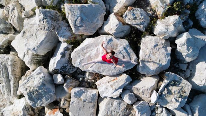 芭蕾舞女演员穿着红裙子在岩石上跳舞。无人驾驶飞机射击。