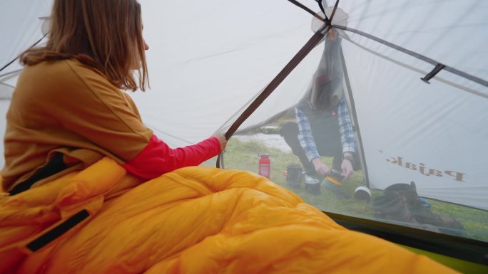 一对浪漫的夫妇穿着暖和的衣服在寒冷的天气里露营。女人拉开帐篷的拉链