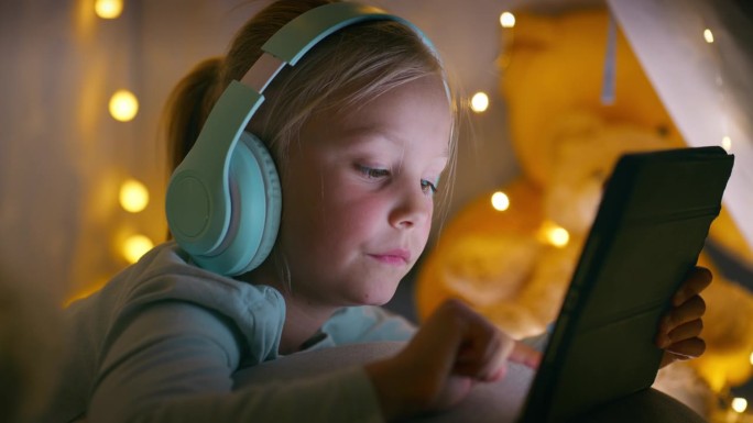 耳机，孩子晚上在家帐篷里用平板电脑打字，社交媒体应用程序，音乐或卡通。科技，女孩或孩子听收音机，听音