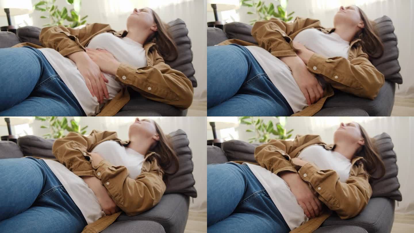 患有月经疼痛的患病年轻女性的选择性焦点。悲伤的女孩用手捏着肚子，胃疼或痛经，躺在家里的沙发上。腹痛概