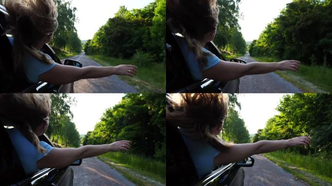 年轻的金发女孩把手伸出车窗，开着车，享受着旅行。一个无忧无虑的女人从车里探出身子，伸出手臂，骑着车穿