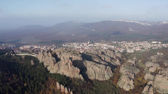 从右到左的扫射显示了Belogradchik雕塑岩石的全景，该镇，背景是保加利亚维丁省的巴尔干山脉。