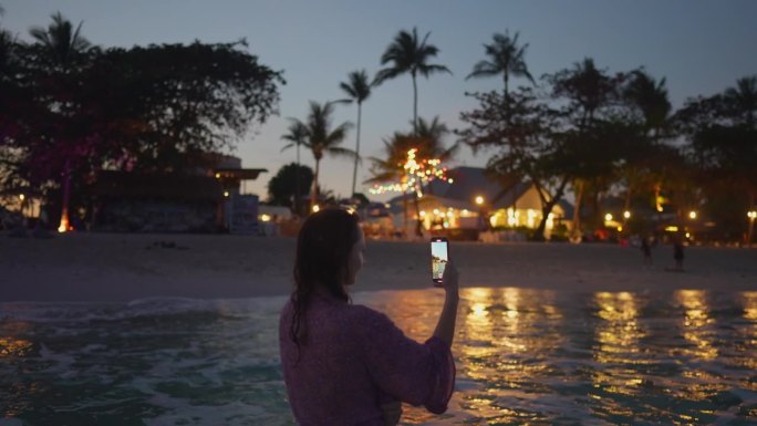 日落后在海滩度假的女人拿着智能手机