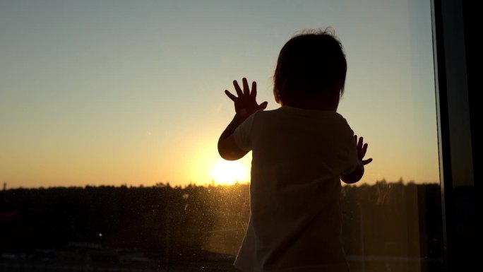 可爱的幼儿女孩在日落背景剪影