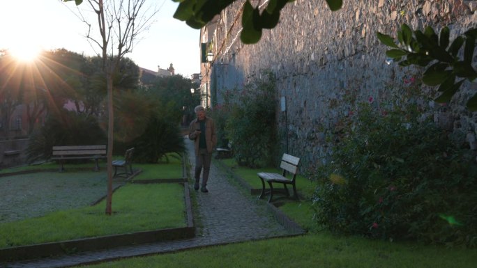 一个成熟的男人沿着历史村庄附近的花园小径走