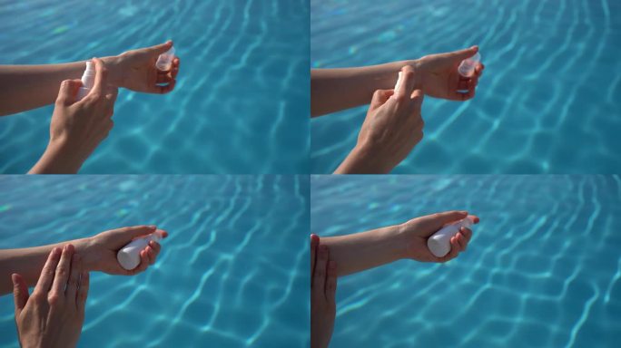 女性手拿一个白色的罐子，在蓝色的泳池水背景上涂抹精华液或油。夏季防晒、保湿、平滑肌肤的概念