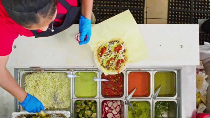 工人在墨西哥餐厅往玉米饼里加配料的俯拍照片