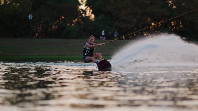 日落时分的女子滑水板运动员。女孩骑在滑水索上。握住牵引绳。夏天在湖里活动。