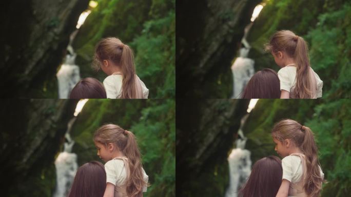 可爱的女孩抱着妈妈看瀑布