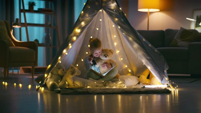 讲故事，手电筒和泰迪熊与一个女孩在她家卧室的帐篷里露营。孩子们，在睡前和孩子一起阅读或看书，亲吻和拥