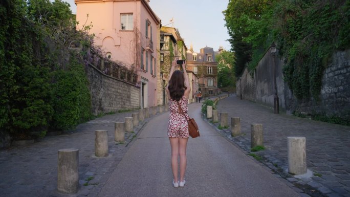 一名女游客穿着可爱的夏装独自在巴黎街头用智能手机拍摄欧洲城市风景，享受假期旅行冒险