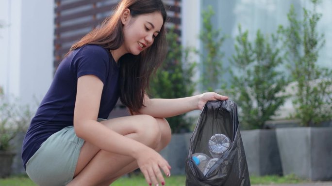 亚洲妇女在家里收集垃圾，拿着装有塑料瓶的回收袋。