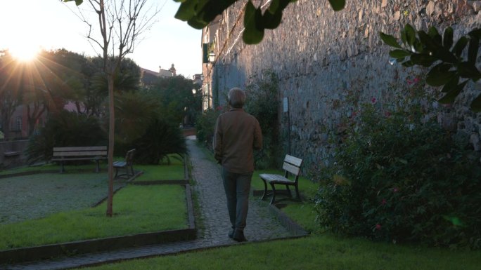 一个成熟的男人沿着历史村庄附近的花园小径走