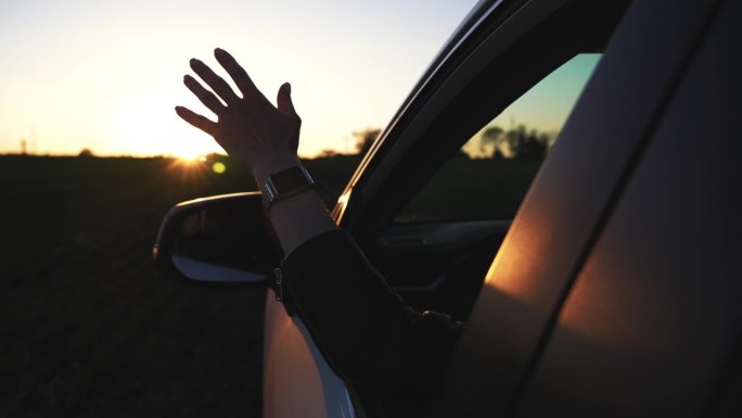 女性开车时手握汽车。女人把手伸出窗外，感受日落时的微风。自由女子手伸出窗外，在耀眼的阳光下开车。汽车