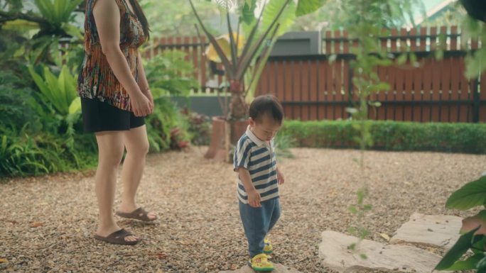 一位亚洲母亲和她的小儿子在后院跑来跑去，一起玩耍。