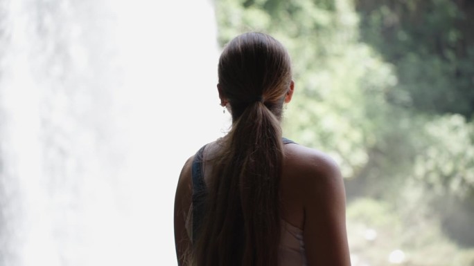 一位身穿牛仔连衣裙的年轻女子正在欣赏森林中山间河流中的瀑布。