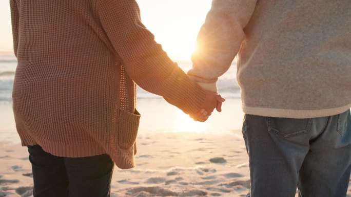 日落、沙滩和一对夫妇在海边牵手的特写，这是为了承诺、纽带和爱的美好时光。结婚、旅游、男女在假日、假期
