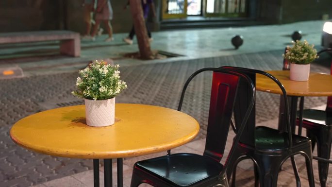 傍晚，街边咖啡馆里的空黄桌装饰花盆的特写。背景中汽车经过铺着石板的道路