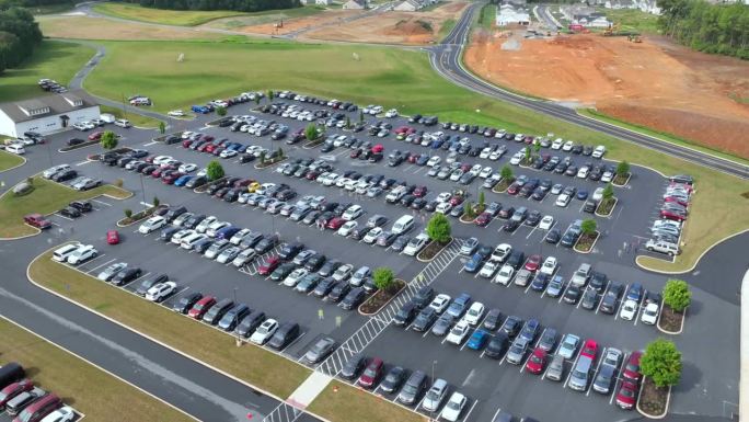 汽车和人进出美国的大型沥青停车场。现场直播，还有穿着黄色背心的停车人员。空中hyperlapse。交