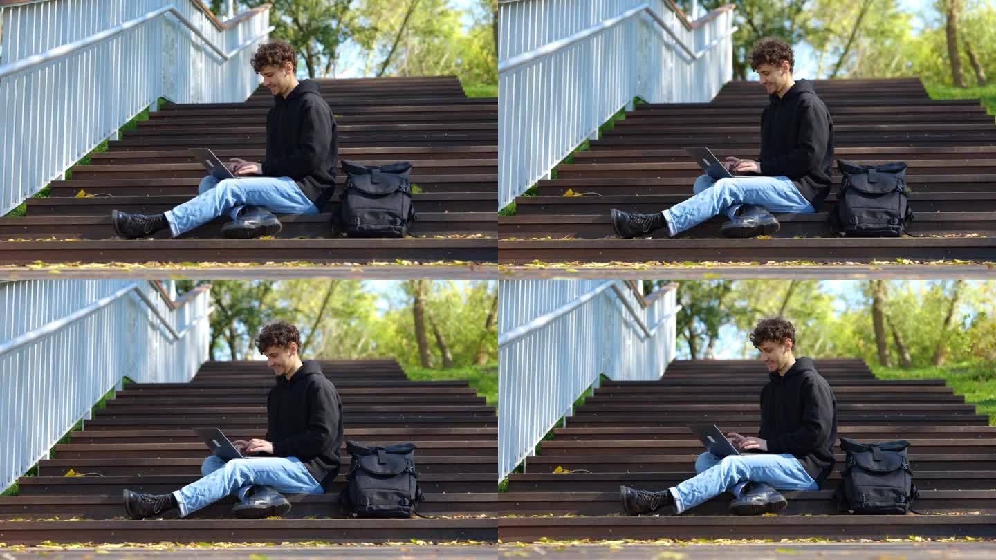 一个快乐的人坐在公园的楼梯上，一边用笔记本电脑打字。秋天的季节。教育，工作理念。实时概念。