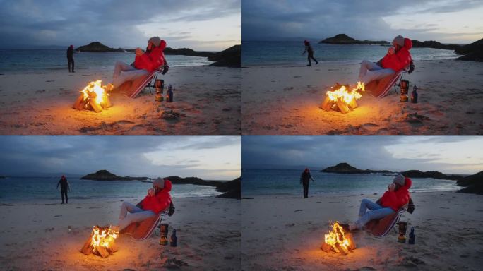 一对浪漫的夫妇穿着暖和的衣服在寒冷的天气里露营。在沙滩上用营火热身