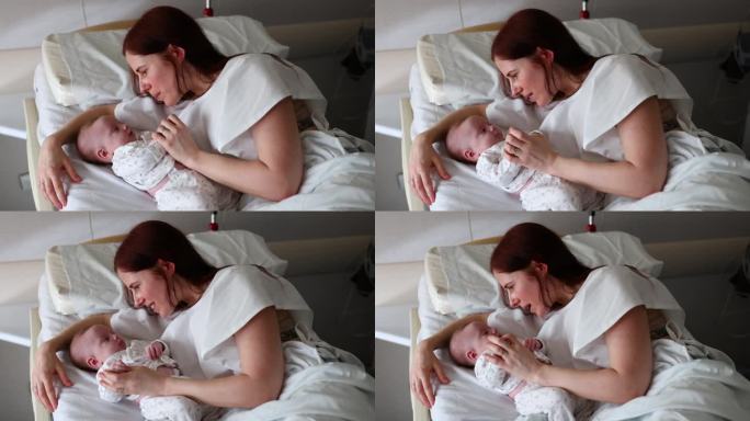 美丽的母亲躺在医院的病床上和她的女婴开玩笑地说话