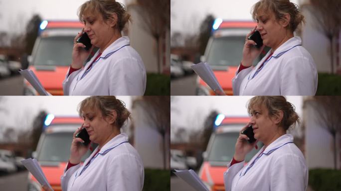 一位穿白大褂的医生站在街上用手机打电话。背景中有一辆救护车。