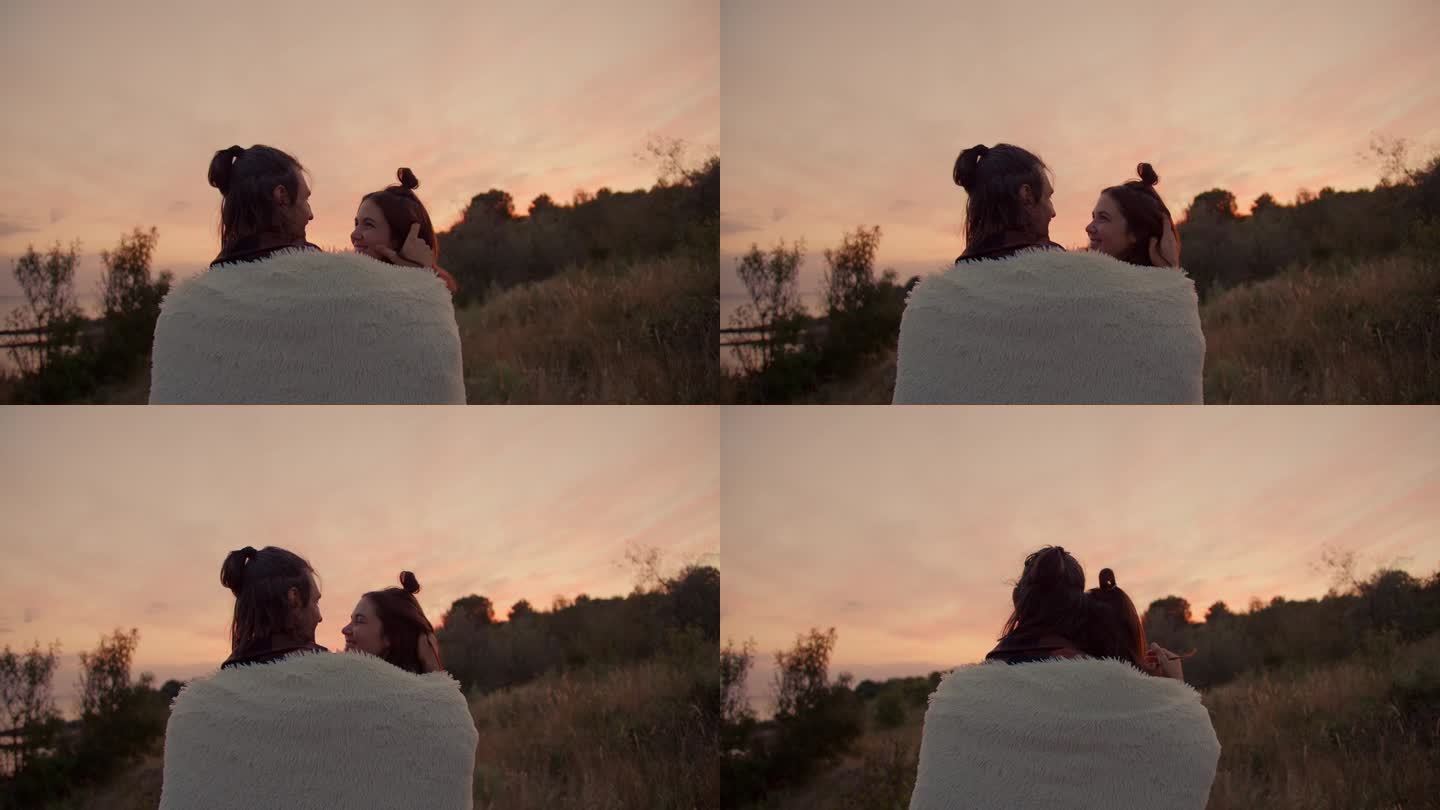 从背后拍摄:一对相爱的情侣，盖着毯子，拥抱着看日落。在城外安静地休息。在乡间别墅休息