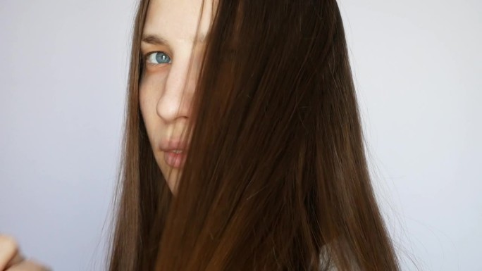 一个美丽的黑发女孩的特写，在白色的背景下用木梳子梳理她的长发