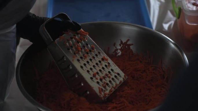 一位妇女在磨碎器上擦胡萝卜