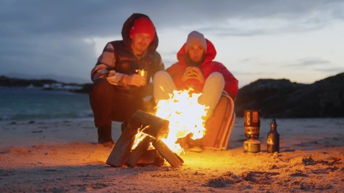 一对浪漫的夫妇穿着暖和的衣服在寒冷的天气里露营。在营火旁热身
