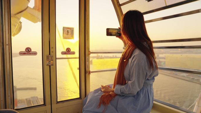 日落时分，女游客在大阪码头摩天轮上欣赏美景