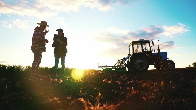 男农民和女农艺师在春天的早晨，拖拉机在农田上播种，种植小麦、黑麦等粮食作物